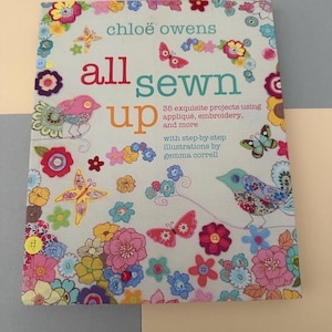 May include: A book by Chloe Owens, titled "all sewn up", with a cover adorned with floral and butterfly illustrations. The text reads "35 exquisite projects using appliqué, embroidery, and more".