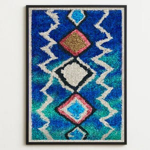 Könnte beinhalten: Gerahmtes abstraktes Kunstwerk mit geometrischem Design. Das Kunstwerk zeigt ein strukturiertes, farbenfrohes Muster in Blau-, Türkis-, Rosa- und Goldtönen mit weißen Zickzacklinien. Das Stück ist in einem schwarzen Rahmen eingefasst.