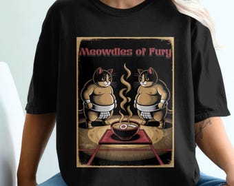 Puede incluir: Camiseta negra con un gráfico de dos gatos con trajes de lucha de sumo. El texto "Meowdles of Fury" está por encima de los gatos. Los gatos se enfrentan y tienen un tazón de ramen entre ellos.