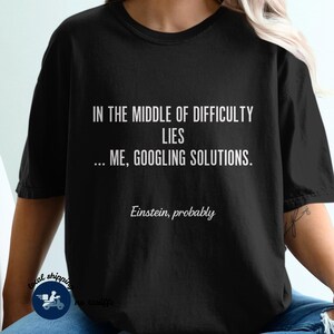 Puede incluir: Camiseta negra con texto blanco: "IN THE MIDDLE OF DIFFICULTY LIES... ME, GOOGLING SOLUTIONS." Debajo, "Einstein, probably." Una camiseta informal y divertida.