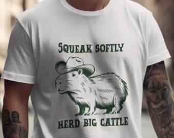 May include: White t-shirt with a green graphic of a capybara wearing a cowboy hat. The text "Squeak Softly Herd Big Cattle" is printed below the image.