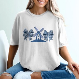 May include: A white t-shirt with a blue windmill and three blue bows on the front.
