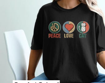 May include: Black t-shirt with a retro design featuring a peace sign, heart, and cat. The text "Peace Love Cat" is printed below the icons. The shirt is made by Comfort Colors.