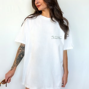 May include: White oversized t-shirt with the text "Five O'Clock Cocktail Club" printed on the front.