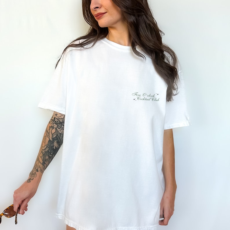 May include: White oversized t-shirt with the text "Five O'Clock Cocktail Club" printed on the front.