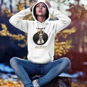 Puede incluir: Sudadera con capucha blanca con un círculo negro y un gráfico de llave dorada. El texto "I unlock your hidden potential" está impreso debajo del gráfico.
