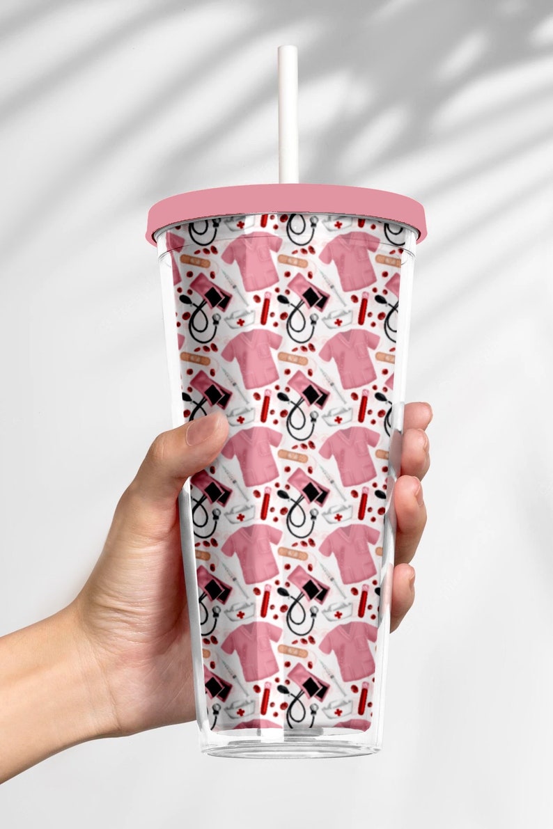 May include: A pink and white reusable tumbler with a straw. The tumbler has a pattern of medical symbols, including a stethoscope, a bandage, a syringe, and a blood pressure cuff.