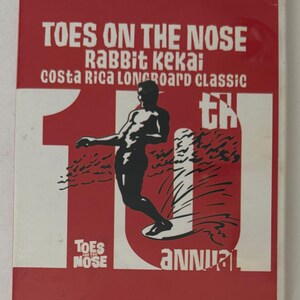 May include: A red DVD case with white text and graphics. The title "TOES ON THE NOSE" is at the top, with "Rabbit Kekai" and "Costa Rica Longboard Classic" below. A black silhouette of a surfer is in the center. The text "10th Annual" is also visible.