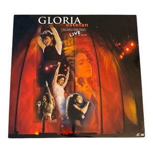May include: DVD case featuring Gloria Estefan's "The Evolution Tour Live in Miami." The cover displays multiple images of Estefan performing on stage, with a red and orange background. The title and artist's name are prominently displayed in white.