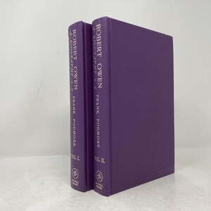 May include: Two purple hardcover books titled "Robert Owen, A Biography" by Frank Podmore. The books are volumes I and II.