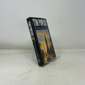 May include: A hardcover book titled "Powers of Two" by Tim Powers. The book has a black spine with the author's name and title in white. The cover features a landscape with tall, pointed structures and a sunset.