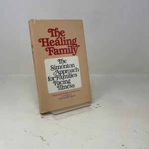 Puede incluir: Un libro de tapa dura con una cubierta beige titulado "The Healing Family". El título está en una fuente roja estilizada. Una etiqueta blanca en la portada dice "The Simonton Approach for Families Facing Illness".