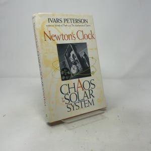 May include: A hardcover book titled Newton's Clock: Chaos in the Solar System by Ivars Peterson. The cream-colored cover features a central black and white illustration of a clock mechanism surrounded by thin yellow orbital lines and text.