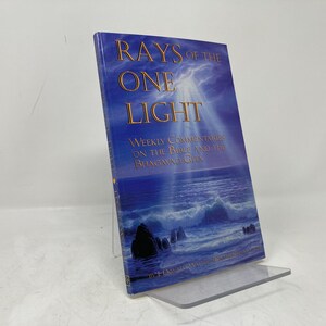 Peut inclure: Un livre intitulé "Rays of the One Light" avec une couverture bleue et blanche représentant un paysage marin. Le sous-titre du livre est "Commentaires hebdomadaires sur la Bible et la Bhagavad Gita."