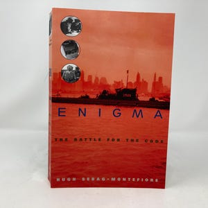 May include: A red book cover with the title "ENIGMA THE BATTLE FOR THE CODE" and the author "HUGH SEBAG-MONTEFIORE". The cover features a black and white photo of a ship in a harbour with a city skyline in the background.
