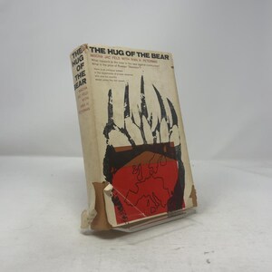 May include: A vintage book titled "The Hug of the Bear" by Mischa Jac Feld with Wan H. Peterman. The cover features a black claw design over a red map, with the title in bold black letters. The book has a worn, aged appearance.