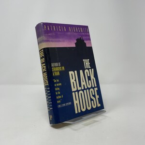 May include: A hardcover book titled "The Black House" by Patricia Highsmith. The book has a dark blue cover with white lettering and a silhouette of a building. The spine reads "The Black House" and "Patricia Highsmith".