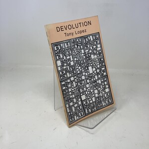Può includere: Un libro intitolato "DEVOLUTION" di Tony Lopez. La copertina presenta un motivo geometrico in bianco e nero su sfondo beige. Il libro è esposto su un supporto in acrilico trasparente.