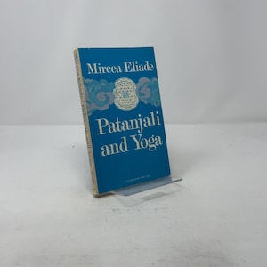 May include: A hardcover book titled "Patanjali and Yoga" by Mircea Eliade. The book has a blue cover with white text and a geometric design. The book is displayed on a clear plastic stand.