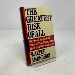 Puede incluir: Un libro de tapa dura titulado "THE GREATEST RISK OF ALL" de Walter Anderson. El libro tiene una cubierta color crema con texto rojo y azul y una banda roja. El libro se exhibe en un soporte de plástico transparente.