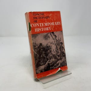 Peut inclure: Un livre vintage intitulé "Concise Dictionary of Contemporary History" avec une couverture rouge et une illustration en noir et blanc d'une scène historique. Le livre est posé sur un support en plastique transparent.