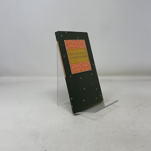 May include: A hardcover book titled "The Rubaiyat of Omar Khayyam" is displayed. The book has a dark green cover with small star-like designs and a rectangular orange and gold label. The book is propped up on a clear acrylic stand.
