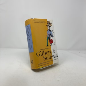 May include: A yellow and blue book cover with a cartoon illustration of a man in a blue uniform holding a walking stick and a red bag. The title of the book is "The Complete Gilbert & Sullivan" with the subtitle "Librettos from all fourteen operettas, complete & unabridged".