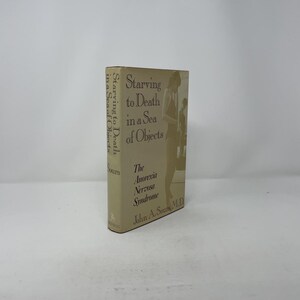 以下が含まれることがあります： ジョン・A・サウルス著「Starving to Death in a Sea of Objects」というタイトルのハードカバー本。本はベージュ色の表紙で、テキストと人物のイラストが描かれています。背表紙には「Starving to Death in a Sea of Objects」と書かれています。