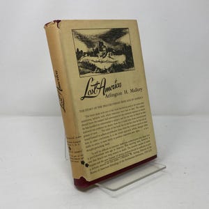 May include: A vintage book titled "Lost America" by Arlington H. Mallory. The book cover features a black and white illustration of a village with a wooden fence and a building with a tall chimney. The text on the back cover describes the book as "The Story of the Pre-Columbian Ruins of America".