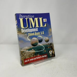 May include: A softcover book titled Iterative UML Development using Visual Basic 5.0 by Jean M. Sekula and Patrick W. Sheridan. The cover features a blue sky, a landscape with water and rocks, three floating spheres, and a CD-ROM included icon.