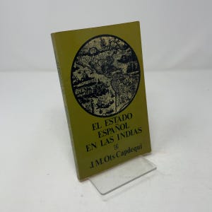 May include: A book with a mustard-yellow cover featuring a circular black and white map illustration. The title EL ESTADO ESPAÑOL EN LAS INDIAS and the author J.M. Ots Capdequí are printed in black text on the front cover of the book.