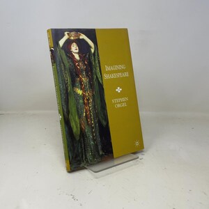 May include: A hardcover book titled "Imagining Shakespeare" by Stephen Orgel. The cover features a painting of a woman in a green and gold gown holding a crown. The background is a mustard yellow.