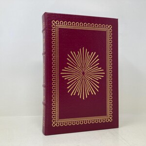 Può includere: Un libro rilegato in bordeaux con un design a stella dorata sulla copertina. Il libro ha un bordo dorato intorno alla copertina e un titolo dorato sul dorso.