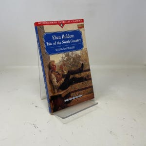 Puede incluir: Un libro de bolsillo titulado "Eben Holden: Tale of the North Country" de Irving Bacheller. La portada presenta una pintura de un hombre relajándose en una valla. El libro forma parte de la serie Wordsworth American Classics.