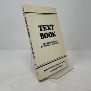 May include: A softcover book titled TEXT BOOK: AN INTRODUCTION TO LITERARY LANGUAGE by Robert Scholes, Nancy R. Comley, and Gregory L. Ulmer. The cover is off-white with bold black text and horizontal black lines at the top and bottom edges.