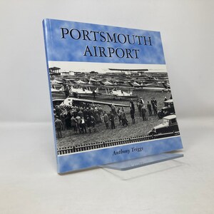May include: A book titled "Portsmouth Airport" by Anthony Triggs. The cover features a black and white photograph of a large group of people standing in front of a field of airplanes.