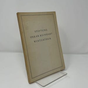 May include: A beige softcover book with a thin black rectangular border on the front cover. The text printed in black on the cover reads STIFTUNG OSKAR REINHART WINTERTHUR. The same text is also printed vertically along the spine of the book.