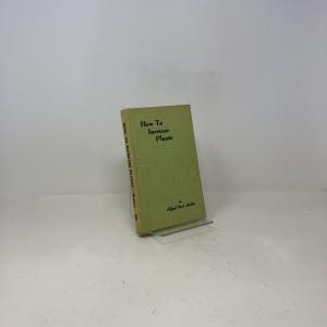 May include: A vintage book titled "How To Increase Plants" by Alfred Carl Hottes. The book has a light green cover with black text. The book is propped up on a clear stand against a white background.