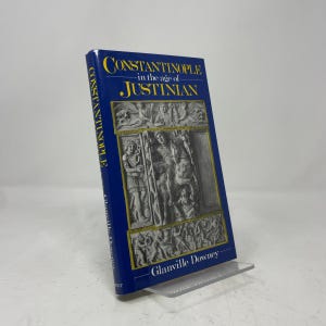 May include: A hardcover book titled Constantinople in the Age of Justinian by Glanville Downey. The cover is deep blue with yellow text and features a central rectangular illustration of a grey stone relief carving depicting historical figures.