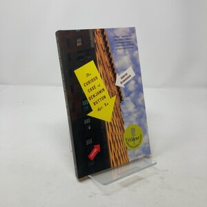 May include: A book cover with a yellow arrow pointing to a building. The title is "The Curious Case of Benjamin Button, Apt. 3c" by Gabriel Brownstein. The book is a winner of the Hemingway/Capote Award for Fiction.