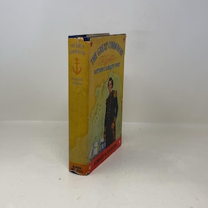 Puede incluir: Un libro antiguo de tapa dura titulado "The Great Commodore: The exploits of Matthew Calbraith Perry" de Edward M. Barrows. El libro tiene una cubierta amarilla con una ilustración de un oficial naval y un mapa.