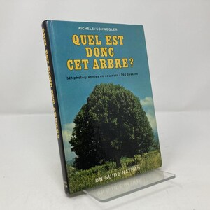 Puede incluir: Un libro en francés titulado "QUEL EST DONC CET ARBRE?" con una portada azul y texto amarillo. La portada presenta una ilustración de un árbol. El libro está apoyado en un soporte transparente.