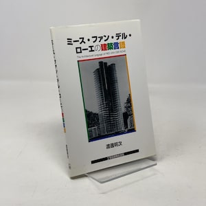 May include: A white book with Japanese and English text. The title is "ミース・ファン・デル・ローエの建築言語" and the subtitle is "The Architectural Language of MIES VAN DER ROHE." The cover shows a high-rise building. The book is on a clear plastic stand.