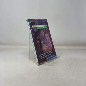 Puede incluir: Un libro de bolsillo titulado "Understanding the I Ching" se muestra en un soporte transparente. La portada presenta un fondo oscuro y texturizado con una imagen de estilo acuarela de dos figuras. El título y el autor son visibles.