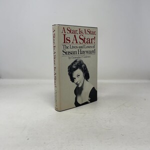 May include: A hardcover book titled "A Star, Is A Star, Is A Star!" featuring a black and white portrait of Susan Hayward. The book's cover is off-white with red and black text. The spine also has text.