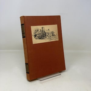 May include: A vintage book with a brown cover and a sepia-toned illustration of a house. The book's spine is a lighter brown, and the title is visible in gold lettering. The book is displayed on a clear stand.