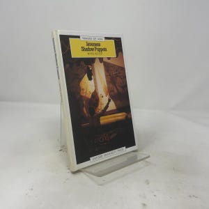 Könnte beinhalten: Ein Taschenbuch mit dem Titel Javanese Shadow Puppets von Ward Keeler aus der Reihe Images of Asia, herausgegeben von Oxford University Press. Das Cover zeigt eine dunkle Illustration einer Schattenspielaufführung mit gelbem Banner.