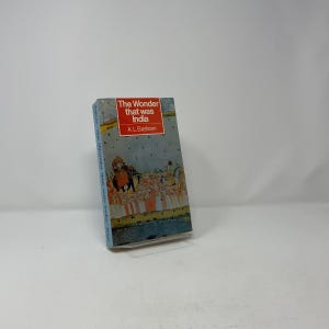 May include: A paperback book titled The Wonder that was India by A.L. Basham. The cover features a red rectangular box with white text, an illustration of an elephant with a decorative carriage, and a light blue background with small dark dots.