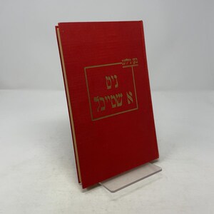 Peut inclure: Un livre à couverture rigide rouge avec des lettres dorées. Le livre est posé sur un support transparent. Le texte sur la couverture est dans une langue étrangère, avec un cadre rectangulaire autour du texte central.
