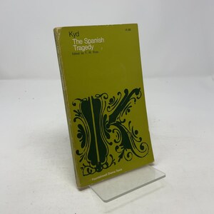 Può includere: Un libro tascabile vintage intitolato "The Spanish Tragedy" di Kyd, curato da T.W. Ross. Il libro ha una copertina verde con una grande "K" decorativa verde scuro e testo. Il libro è esposto su un supporto in acrilico trasparente.